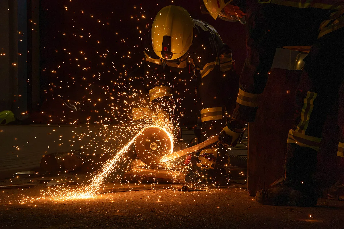 Feuerwehrmann trennt bei Dunkelheit mit dem Trennschleifer ein Werkstück, Funken sprühen über den Boden