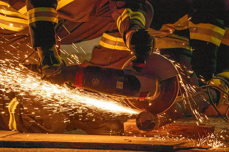 Feuerwehrleute führen gemeinsam einen Schnitt, Funkenregen im Dunkeln
