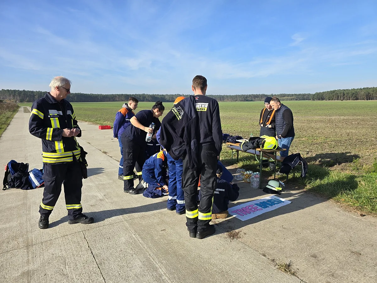 Eine Gruppe der Jugendfeuerwehr an einer Station auf einem Feldweg, Ausrüstung liegt bereit