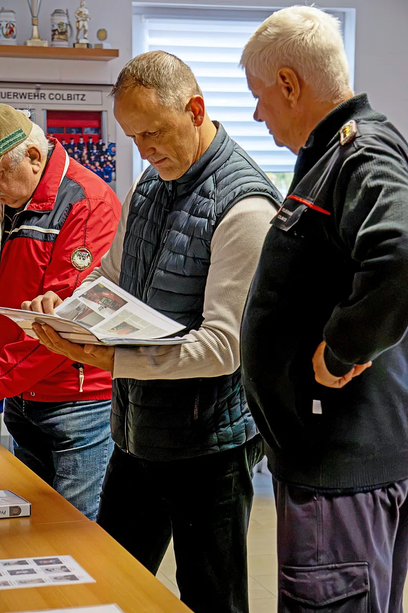 Drei Männer blättern in einer Broschüre an einem Tisch im Gerätehaus