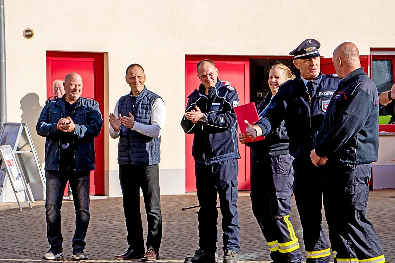 Feuerwehrleute und Gäste stehen applaudierend vor den roten Toren des Gerätehauses