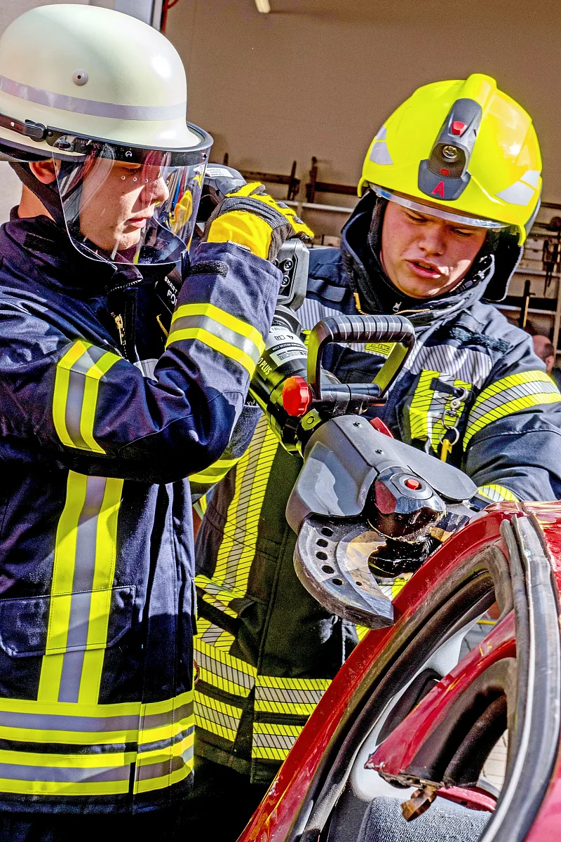 Zwei Feuerwehrleute mit Helm setzen die Rettungsschere an einer Autotür an