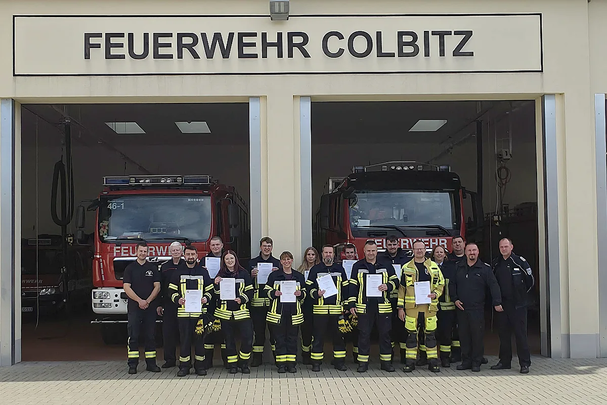 Die Absolventinnen und Absolventen der Truppmannausbildung mit ihren Urkunden und den Ausbildern vor den geöffneten Toren des Gerätehauses der Feuerwehr Colbitz