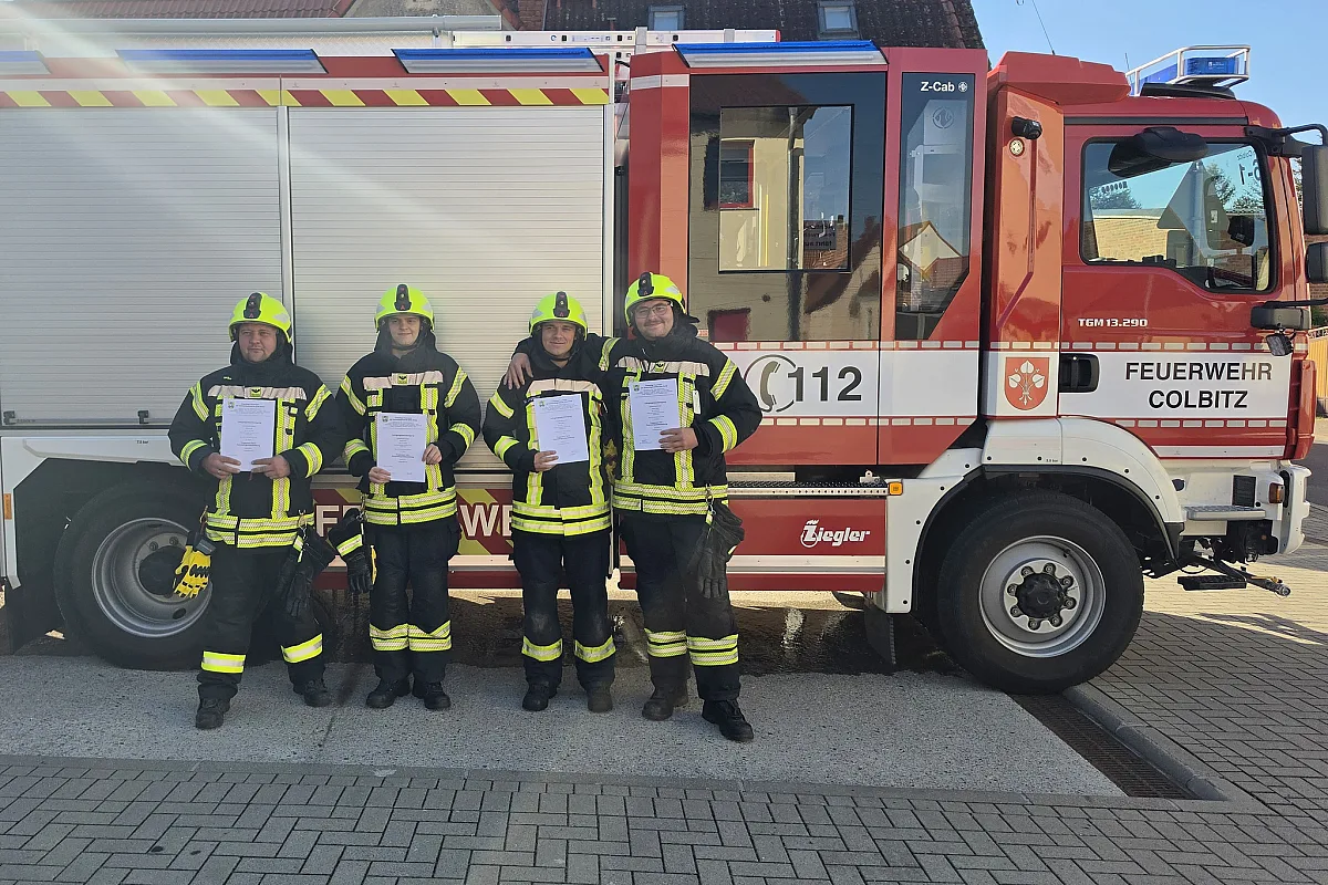 Vier Feuerwehrleute in Einsatzkleidung mit ihren Urkunden vor dem HLF der Feuerwehr Colbitz